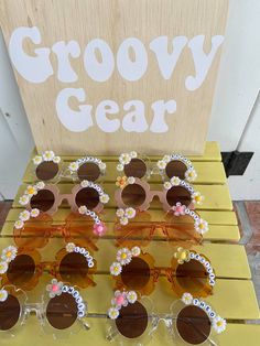 several pairs of sunglasses with flowers on them are sitting on a yellow shelf next to a sign that says groovy gear