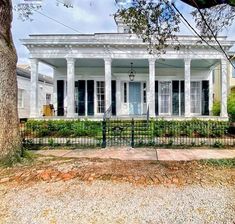 an old white house with columns and pillars on the front porch, surrounded by trees