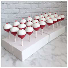 there are many red and white cake lollipops lined up on the table