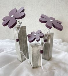 three wooden vases with purple flowers in them on a white cloth covered bed sheet