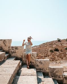 a woman sitting on some stone steps by the ocean with her hand in her hair