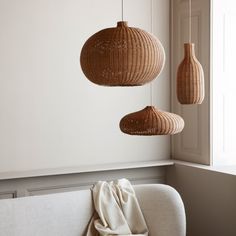 three wicker lamps hanging from the ceiling above a white couch in front of a window