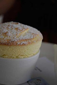 a cake sitting on top of a white bowl filled with powdered sugar covered pastry