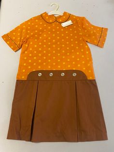 Vintage orange and brown Girls dress with Peter Pan collar and buttons at waist. Polka dot bodice. . Size 10, 32" chest, 30" from top of shoulder to bottom hem. 13.5" shoulder to shoulder, 33" waist. 100% cotton. Old stock with original tags, unworn. Excellent condition! Retro Brown Dress With Buttons, Pan Collar Dress, Peter Pan Collar Dress, Vintage Orange, Brown Girl, Pan Collar, Orange Brown, Peter Pan Collar, Girls Dress