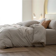 an unmade bed in a bedroom with wooden floors and white walls, along with two lamps