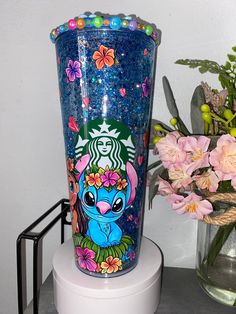 a blue starbucks cup sitting on top of a table next to flowers and a vase