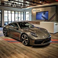 a silver sports car is on display in a showroom with wooden floors and large windows