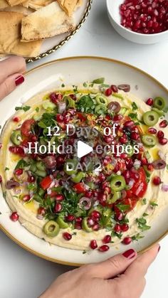 two hands holding a plate with hummus, olives and tomatoes on it that says 12 days of holiday dips