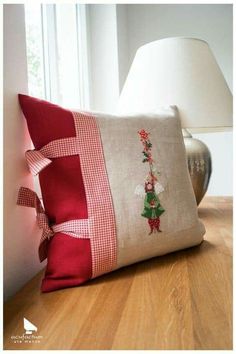 a decorative pillow on a wooden floor next to a lamp with a red and white checkered border