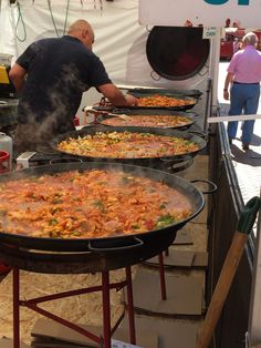 a man cooking food on top of a grill in front of other people at an outdoor event