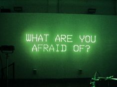 a neon sign that says what are you afraid off? in front of a green wall