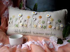 an embroidered pillow with flowers on it next to a cup