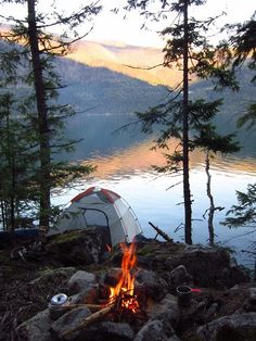 a tent is set up next to a campfire on the shore of a lake