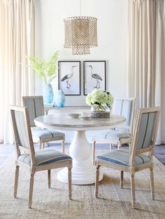 a dining room table with chairs around it and pictures on the wall behind it, along with two vases filled with flowers