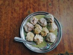 a bowl filled with dumplings on top of a wooden table next to a spoon