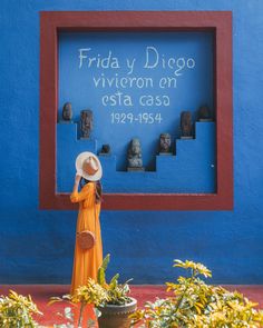 a woman standing in front of a blue wall wearing a white hat and orange dress