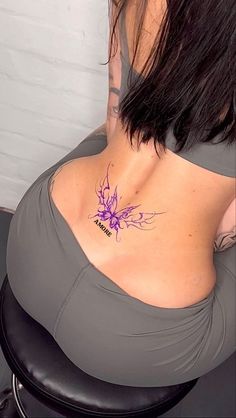 the back of a woman's stomach with a tattoo on her left side and purple flowers