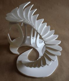 a sculpture made out of white paper on top of a brown surface with the shape of a bird's wing