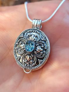 a close up of a person's hand holding a silver locke with a blue stone in it