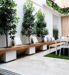 an outdoor dining area with benches and potted trees on the wall, along with artificial grass