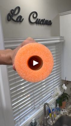 a person holding an orange sponge in front of a kitchen sink with the word la cuana on it