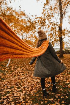 a woman is walking through the leaves with an orange scarf