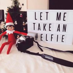 an elf is sitting next to a sign that says let me take an elfie