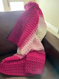 a pink and white crocheted blanket sitting on top of a brown leather couch