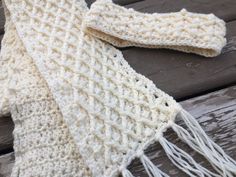 a white knitted scarf sitting on top of a wooden bench