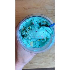 a hand holding a cup filled with blue ice cream on top of a wooden table