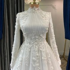 a white wedding dress with long sleeves and flowers on the skirt is displayed in front of a