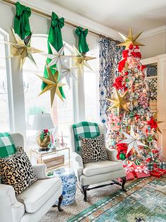 a living room decorated for christmas with green and gold decorations on the walls, white chairs and a large tree