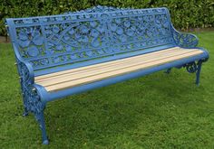 a blue bench sitting on top of a green grass covered park field next to bushes