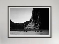 black and white photograph of people riding horses in the desert with mountains behind them, framed on wall