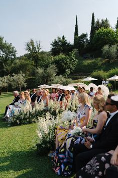 a group of people sitting on top of a lush green field next to umbrellas