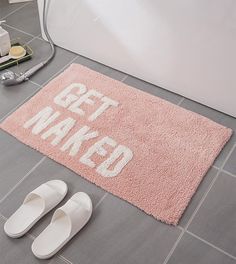 a bathroom rug that says get naked on the floor next to slippers and toilet