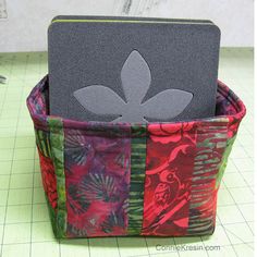 an open laptop computer sitting on top of a colorful patchwork basket with flowers and leaves