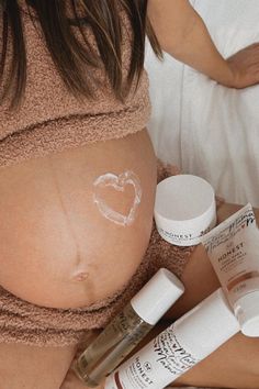 a pregnant woman laying in bed with her stomach covered by creams and other skin care products