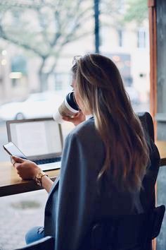 a woman sitting at a table with a cup of coffee in front of her and looking out the window