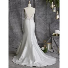 a white wedding dress on a mannequin in front of a gray backdrop with greenery