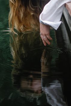 a woman's hand on the edge of a dock next to water with her reflection in the water