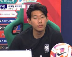 a man sitting in front of a soccer ball on top of a desk next to a microphone