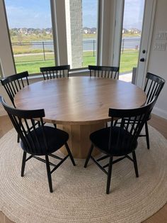 a round table with four chairs in front of two large windows and a rug on the floor