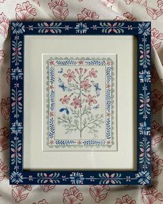 a blue and white frame holding a cross - stitch pattern with pink flowers on it