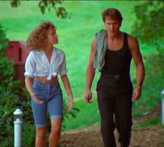 a man and woman walking down a dirt road in front of green grass covered trees