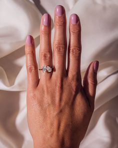 a woman's hand with a pink manicure and ring on it, against a white sheet