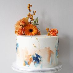 there is a white cake with orange flowers on top and blue paint splatters