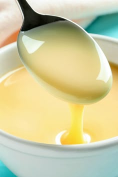 a spoon full of yellow liquid being poured into a white bowl with blue cloths in the background