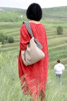 a woman in a red dress is walking through tall grass with a handbag on her shoulder