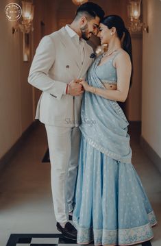 a man and woman standing next to each other in a hallway with chandeliers hanging from the ceiling